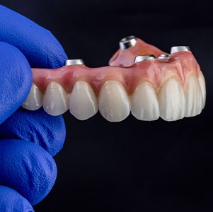 Gloved hand holding implant denture against dark background