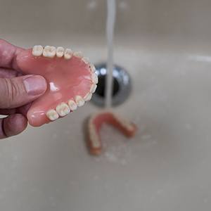 Person rinsing their dentures in bathroom sink